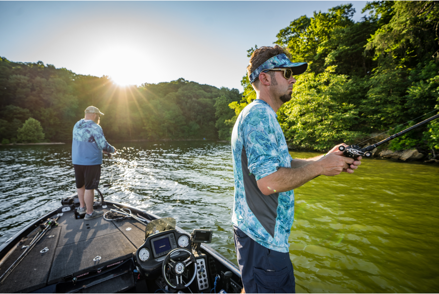 Two men hold fishing poles off a boat in the middle of the river