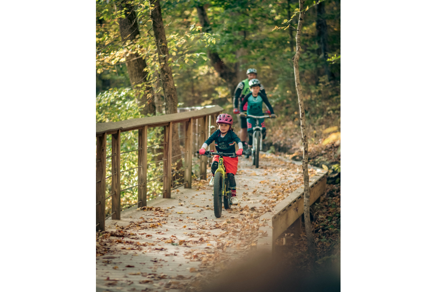 A family mountain biking through a trail in the fall at Clarksville's Rotary Park.