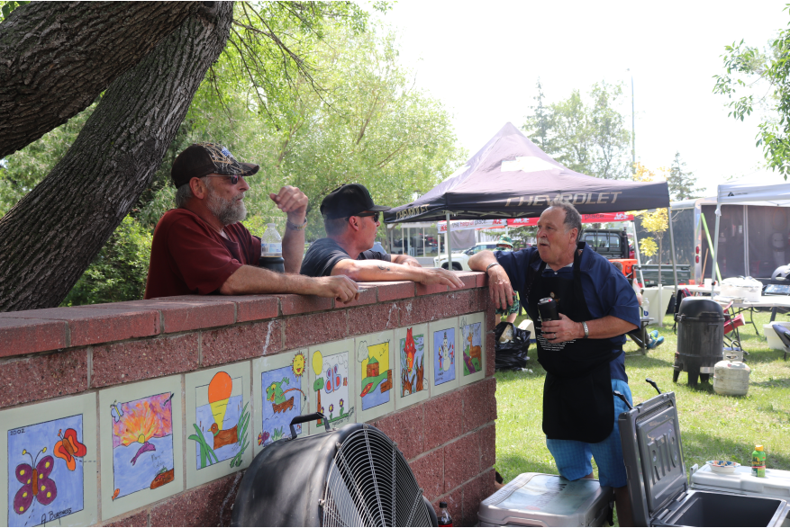 Three men, smiling and talking. Two are leaning against the wall.