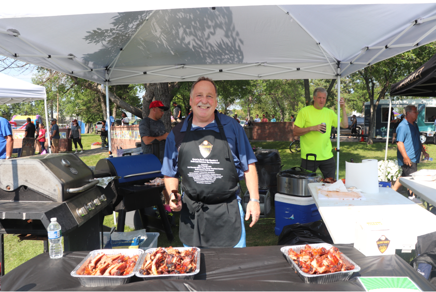 A man smiling with three trays of smoked bbq ribs.