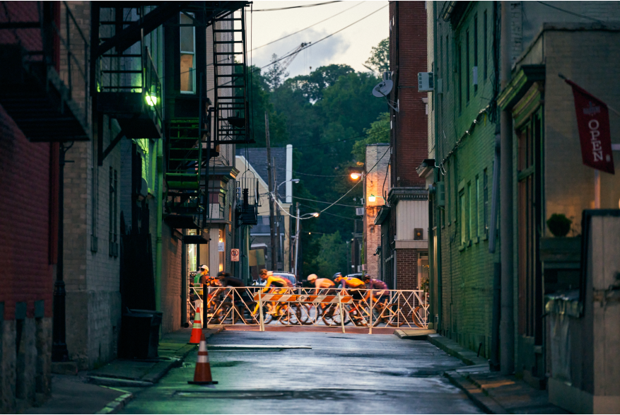Cyclists ride at dusk past an alley during the 2022 Easton Twilight Criterium in Easton, Pa.