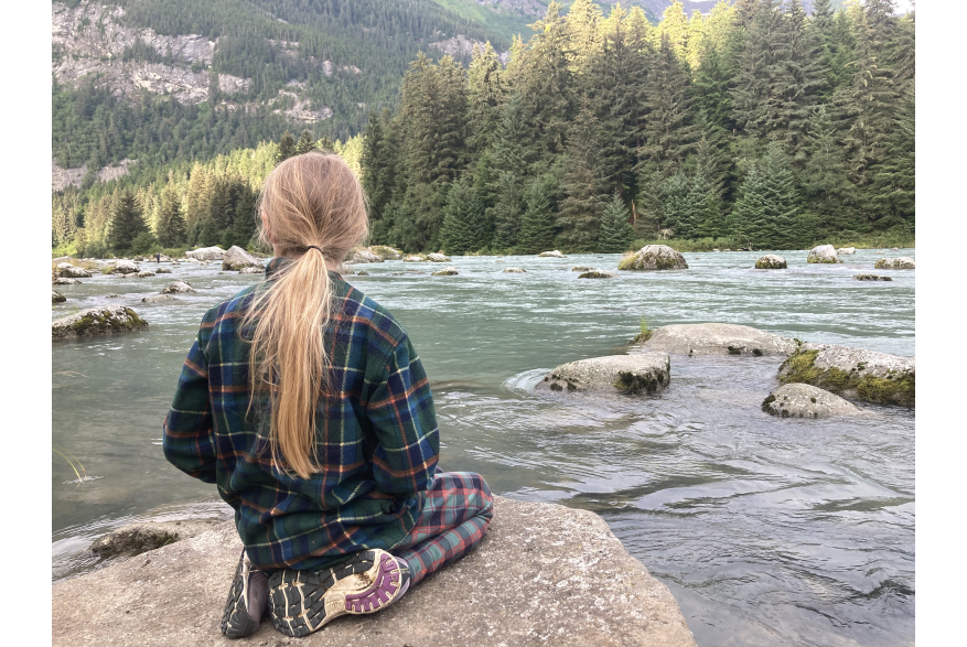 Caught in the tranquility, girl on rock looking at the Chilkoot river