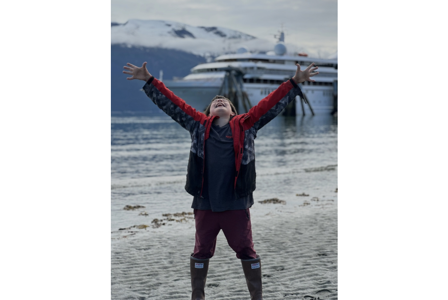 Boy celebrating the sunshine arms raised, cruise ship docked in backdrop