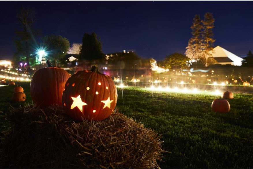 Illuminated pumpkin with star carving sitting on a hay bale