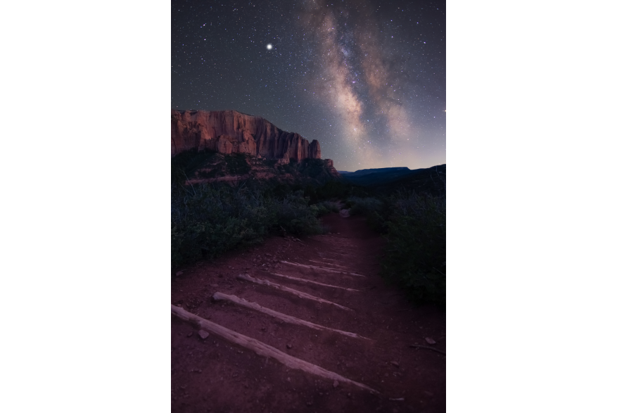 Starry Skies over a dirt hiking trail with logs laid out for steps and towering crimson cliffs in the background in Kolob Canyons, Ut.