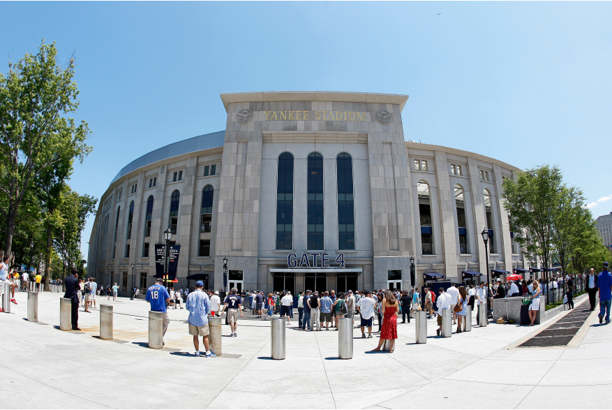 Daytime straight-on view of a Yankees Stadium entrance with a plaza full of fans
