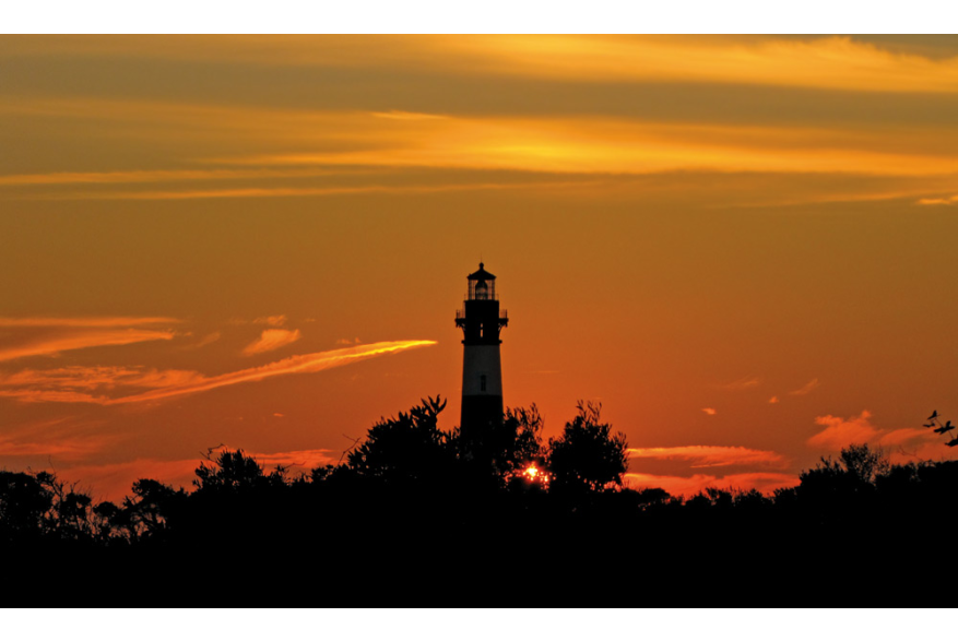 The Bodie Island Lighthouse backlit by an orange sky in Nags Head, NC