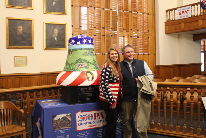 A couple posing in front of a bell at Monroe County's America250PA kick-off event