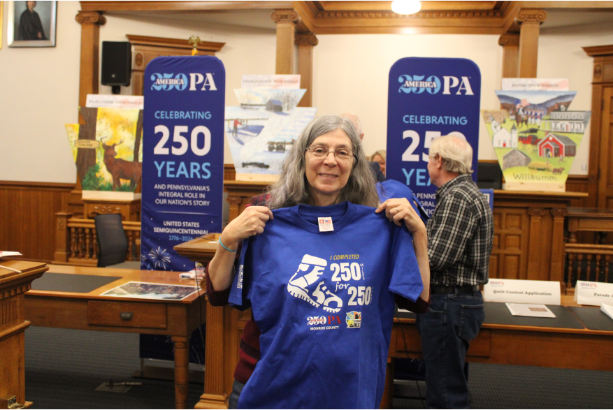 An individual posing with a America250PA shirt at Monroe County's America250PA kick-off event