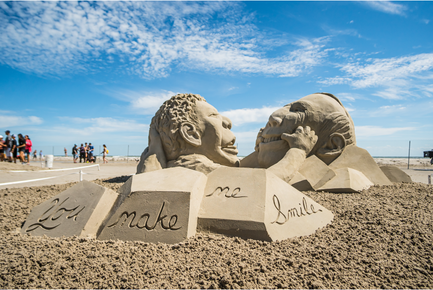 Sand sculpture of child holding mans mouth in a smile.