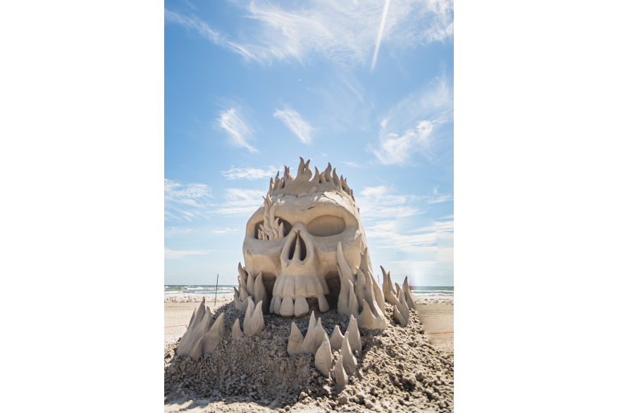 Skull sand sculpture with flames coming through it.