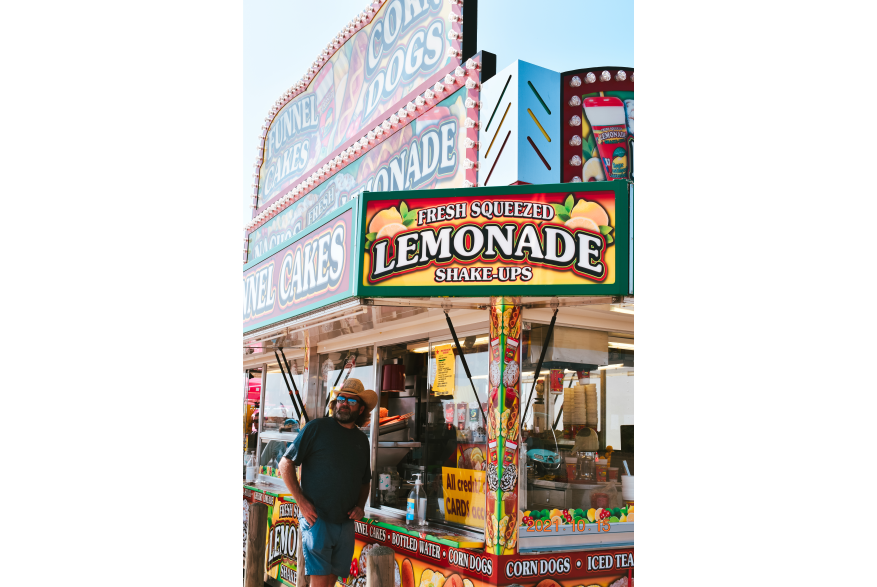 A man stands under a food kiosk that reads lemonade