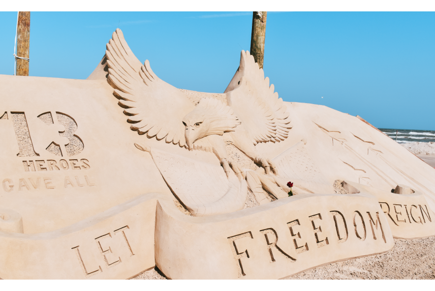 Sand sculpture that says "let freedom reign" with an eagle behind it.