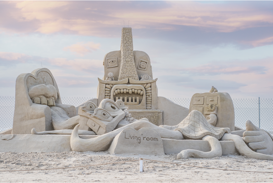 Sand sculpture of a living room with mouths and faces on each ppeice of furniture.