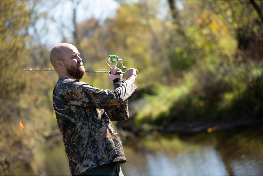 A bearded man wearing camouflage holds a fishing rod.