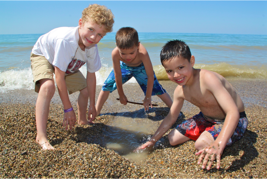 Three young boys play in the sand near the shoreline