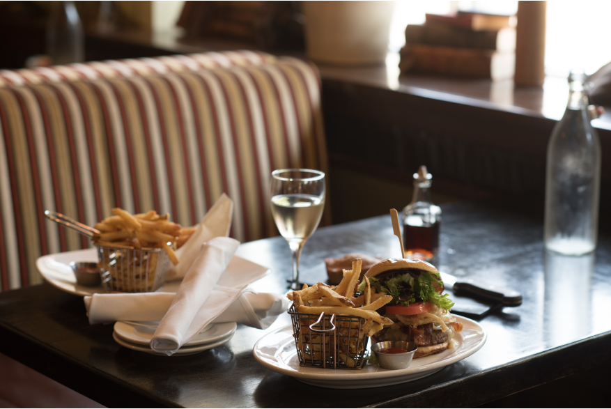 Plates of burgers and fries with a glass of wine on a table