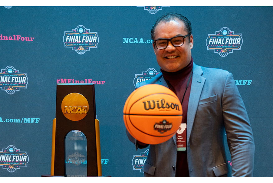 Man holding basketball by NCAA trophy