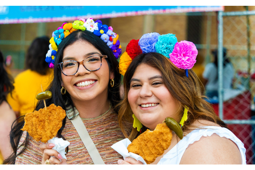 Two girls holding chicken on a stick wearing flower crows at Fiesta San Antonio.