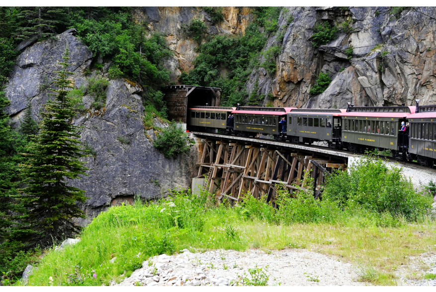 Vintage train cars traversing bridge and entering tunnel
