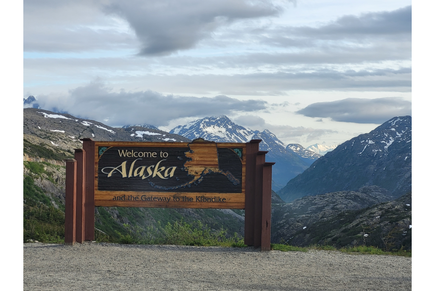 a large brown wooden sign with an outline of the State of Alaska reads "Welcome to Alaska"
