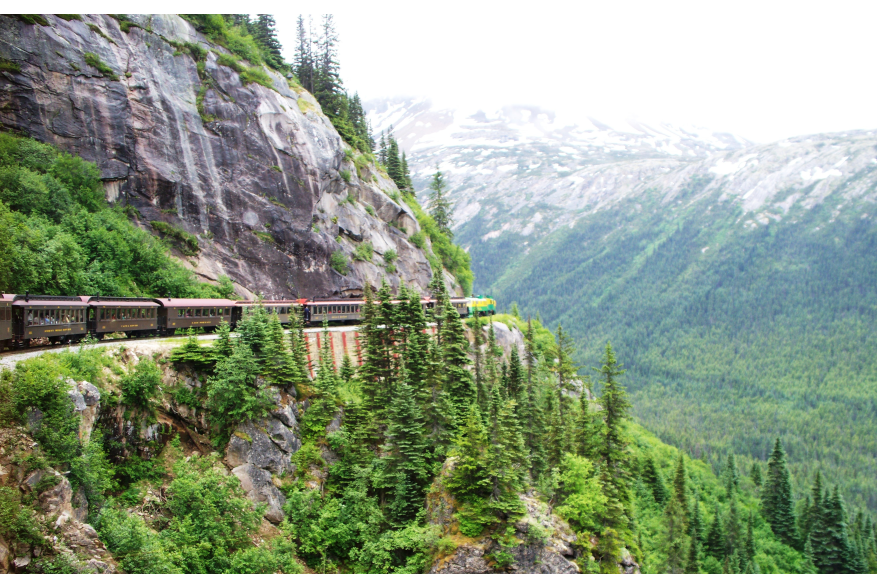 White Pass 90 ceres locomotives pull brown train cars through rocky mountain terrain along the White Pass & Yukon Route