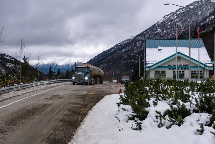 A double tanker truck passing by the US border crossing on gravel covered road with snow on he sides on the way to Canada.