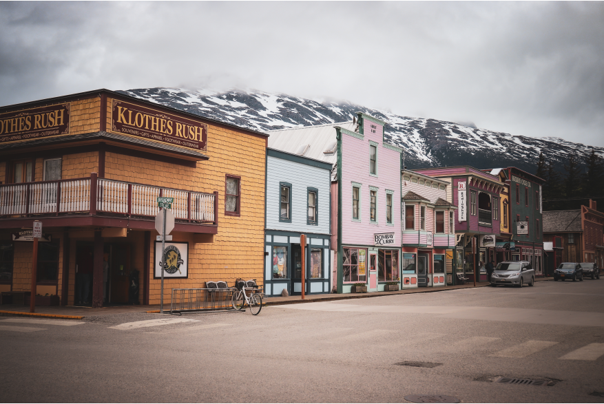 Brightly colored gold rush style false front building line an empty asphalt street on an overcast day in Skagway Alaska. Snow still on the mountains in the back ground. One bicycle in the bike rack on at the intersection