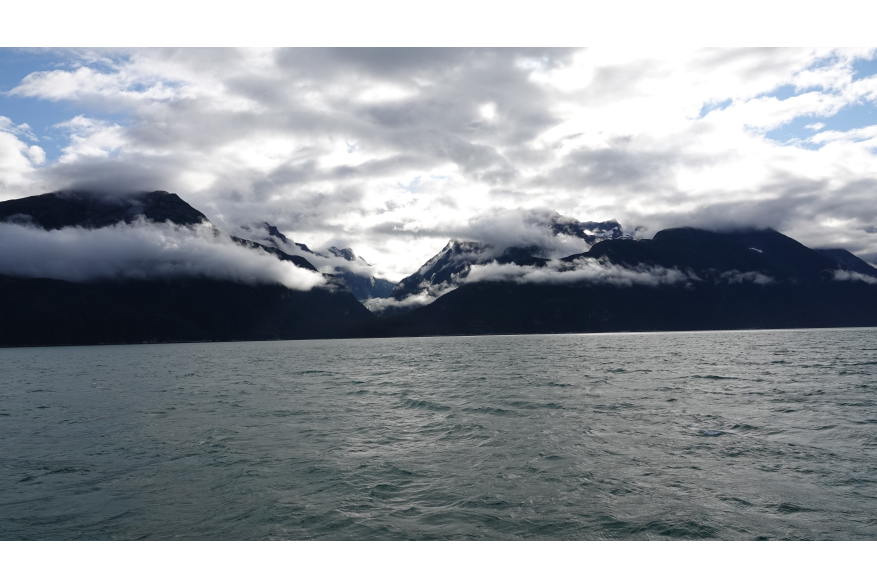 Sunrise coming up over mountain on the Talya Inlet with dramatic low clouds, while in transit to Davidson Glacier.