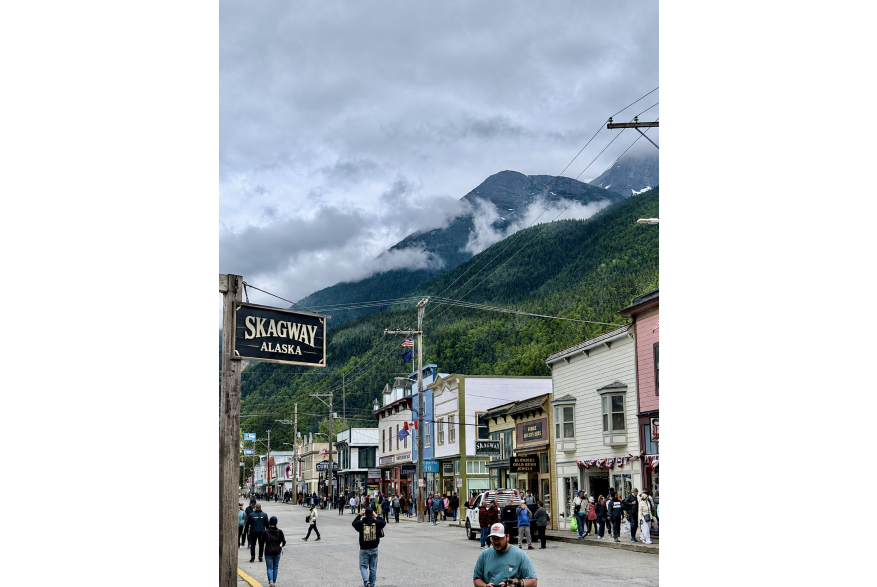 Title: Where the Mountains Meet Main Street Nestled beneath mist-covered mountains, downtown Skagway captures the striking contrast between human history and Alaska’s rugged wilderness. The bustling street, colorful Gold Rush-era storefronts, and gathering visitors reflect the town’s enduring energy, while the towering forested slopes and drifting clouds reveal the powerful landscape that continues to shape it.