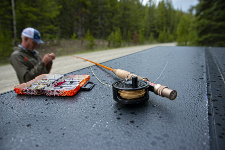 fly fishing line and tackle on a flat surface set in front of a fisherman tying a line