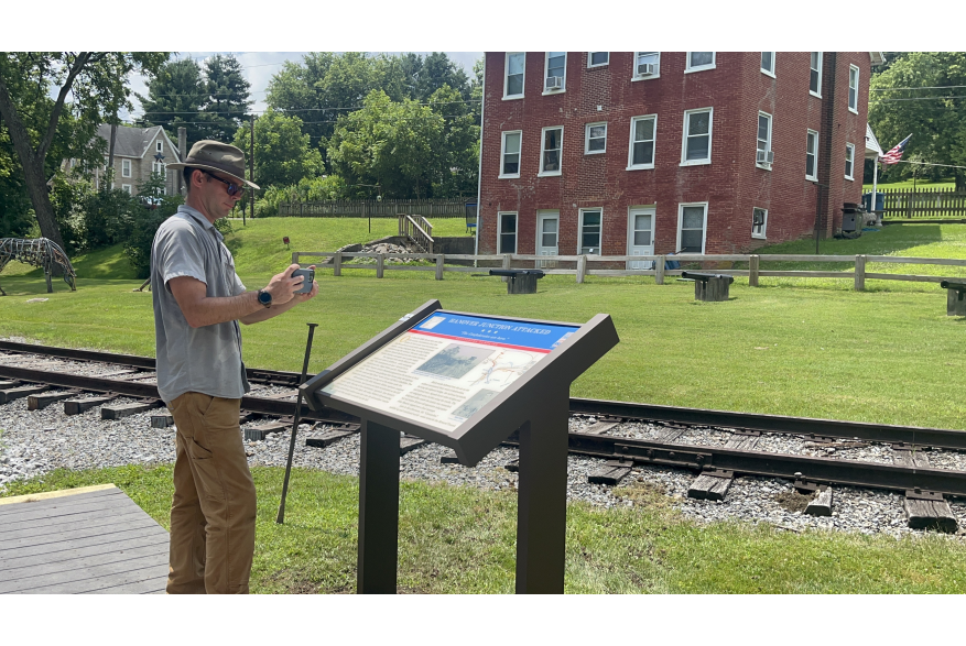 a man taking a photo of the Civil War Trails Marker located at Hanover Junction along the Heritage Rail Trail