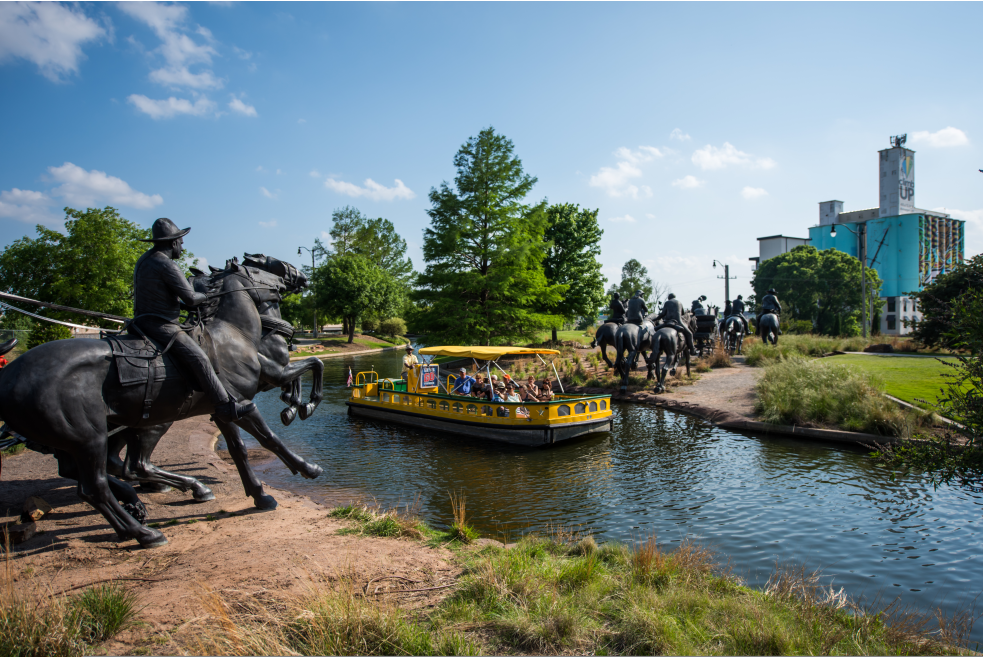 Group of people viewing OKC's Land Run Monument while riding the Bricktown Canal Water Taxi