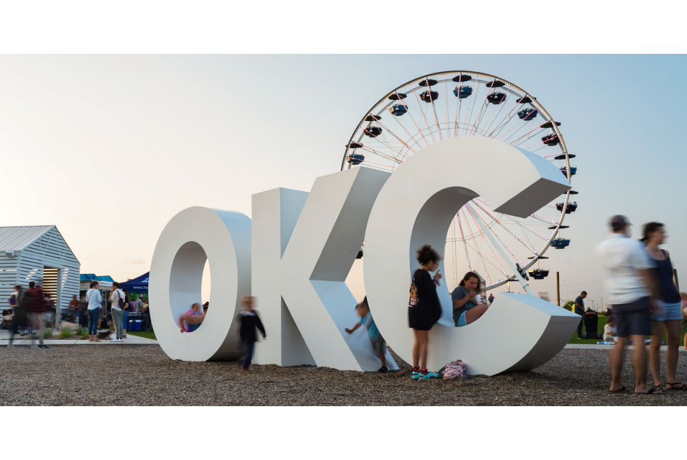 Groups of people enjoying "OKC" sign and Wheeler Ferris Wheel in Oklahoma City's Wheeler District