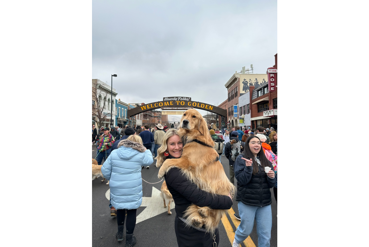 A women holding an adult golden retriever in her arms with the historic welcome to Golden arch in the background