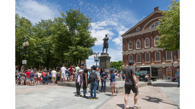 A group of visitors pause at the Samuel Adams statue outside Faneuil Hall