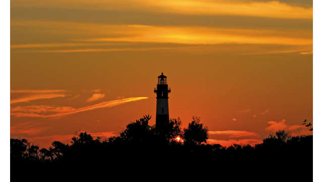 The Bodie Island Lighthouse backlit by an orange sky in Nags Head, NC