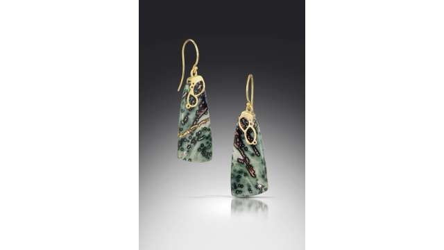 A pair of green stone earrings with small black and brown spots. The setting is gold, making two small loops around the top of the stones before forming the earring hook.
