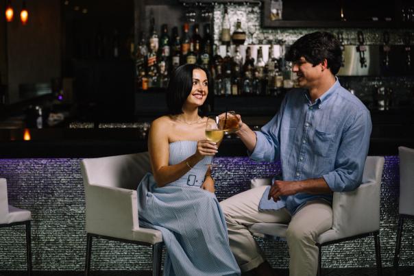 A couple sitting in front of the bar at the White House Hotel, clinking their drink glasses.