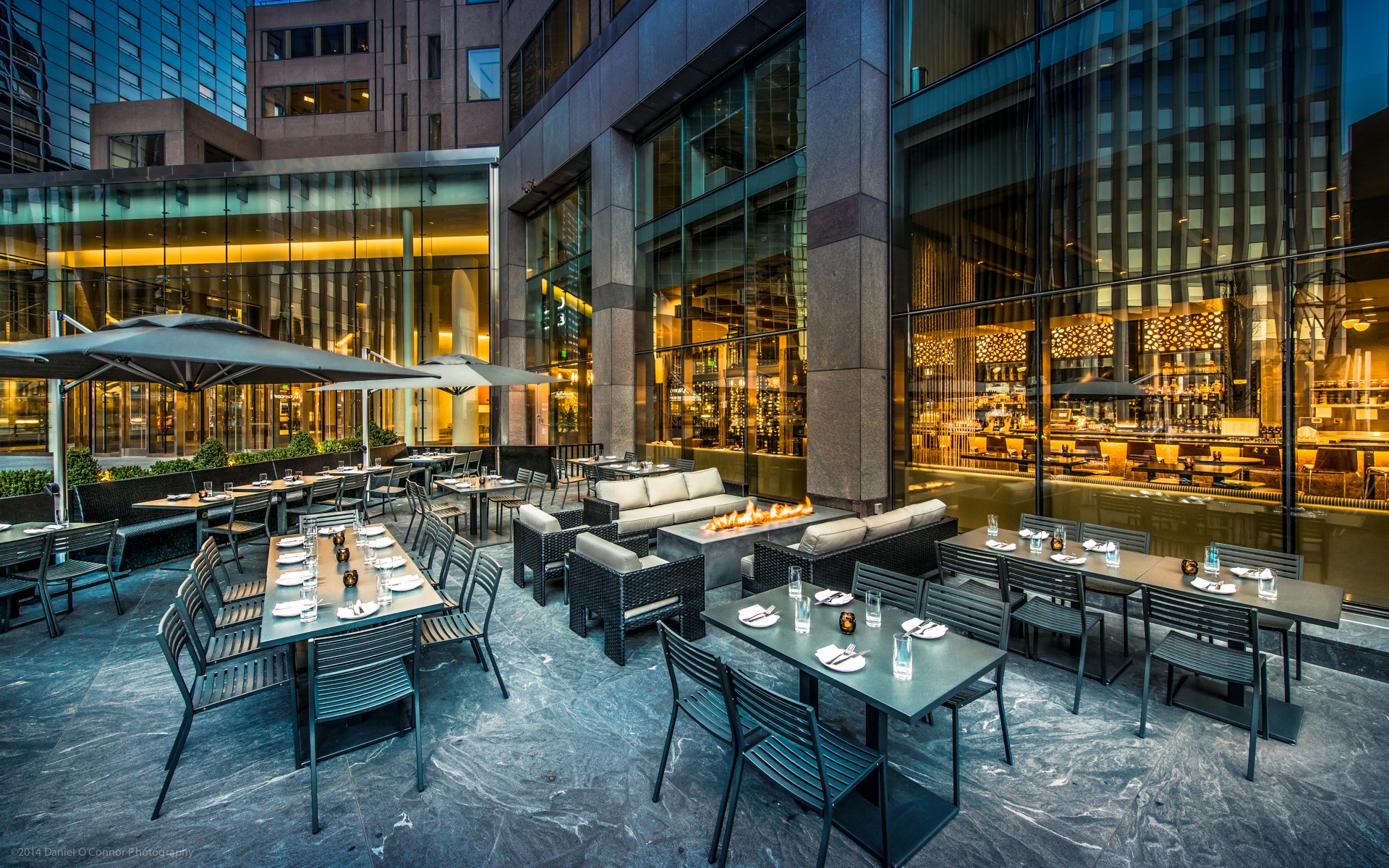 Guard and Grace, Denver, United States outdoor restaurant patio with black tables, chairs, umbrellas, and modern fire pit.