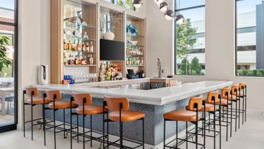 Gbar - This bright, modern bar features a sleek design, surrounded by large windows that fill the space with natural light, and a stylish marble countertop lined with warm, orange barstools. It offers an inviting atmosphere that's perfect for enjoying cocktails and gathering with friends.