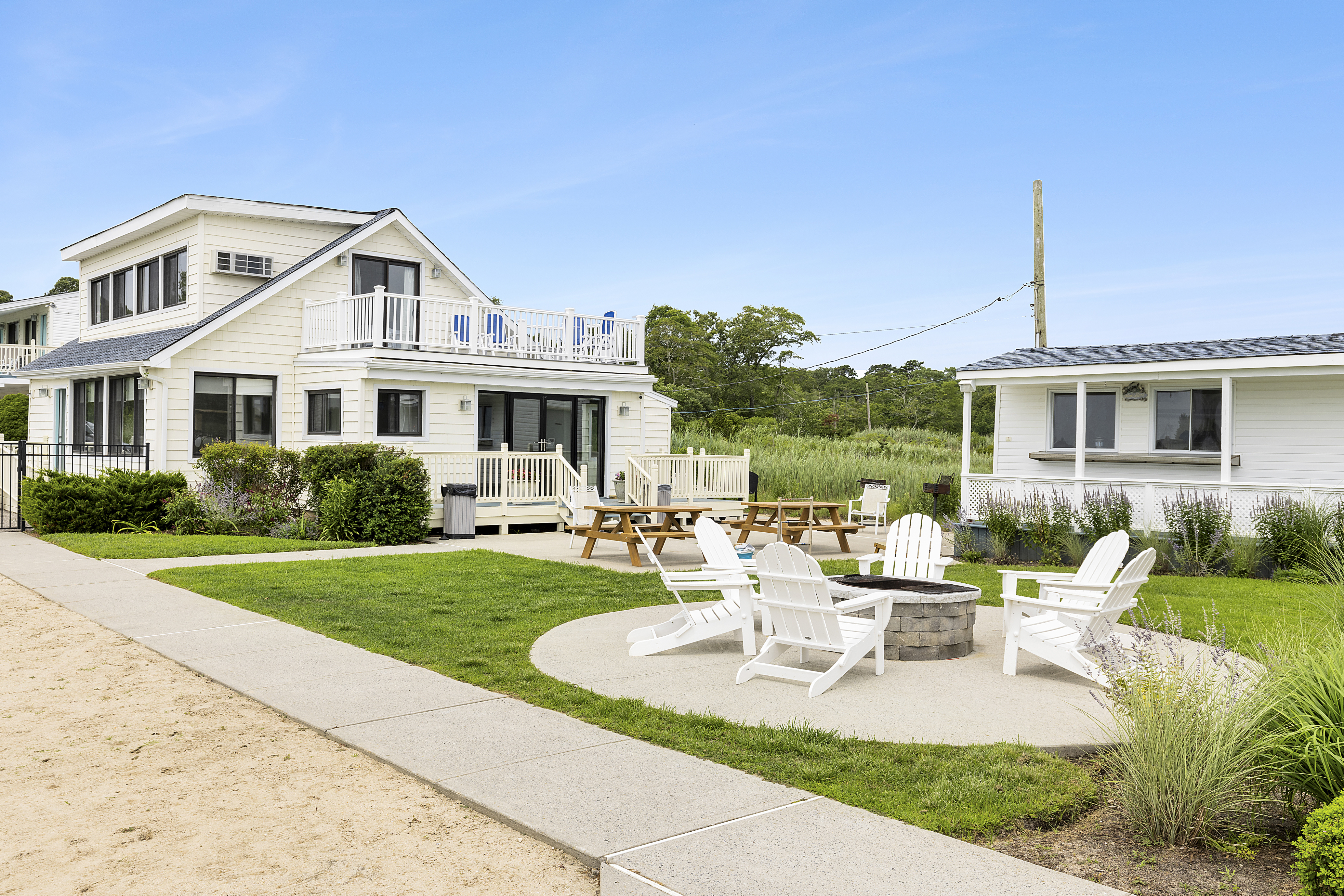 Waterfront Amenities - Clubhouse Exterior - Here is the exterior of our beautiful Clubhouse, which houses our continental breakfast and fitness center. Guests have the option to open the double doors to sit out on one of our picnic benches to enjoy their meal or to soak in the morning rays. The concrete pathway leads to our pool and dock. Our lovely fire pit fitted with adirondack chairs is also featured!