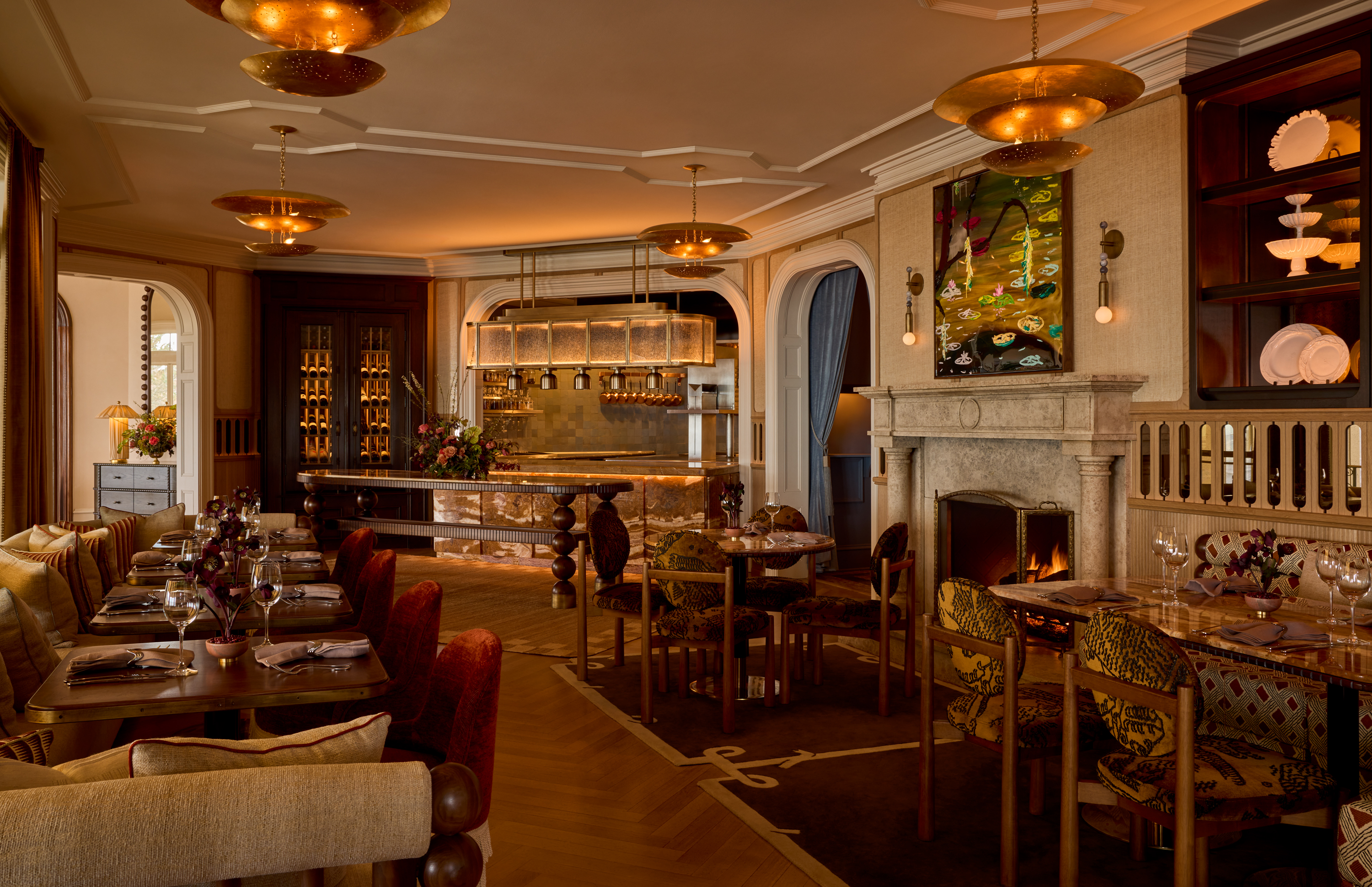 A warmly lit dining area with a fireplace, bar, and several tables set for dinner.