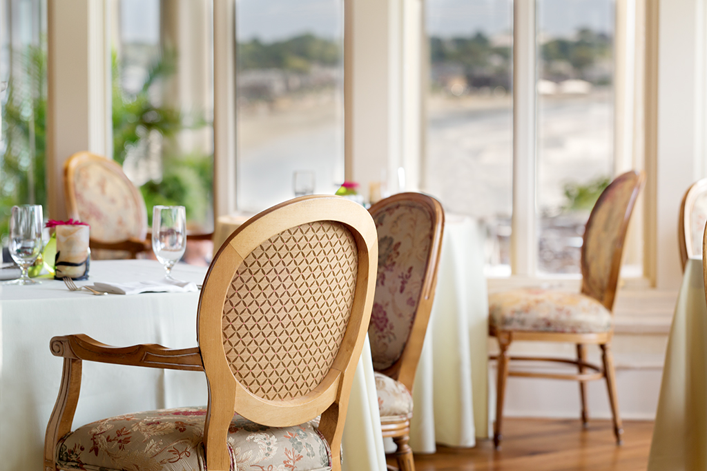 A dining area with a table set for a meal, chairs with floral upholstery, and large windows offering a view.