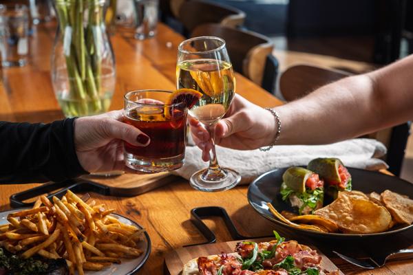 A table with food and drinks, with two people's hands holding glasses.