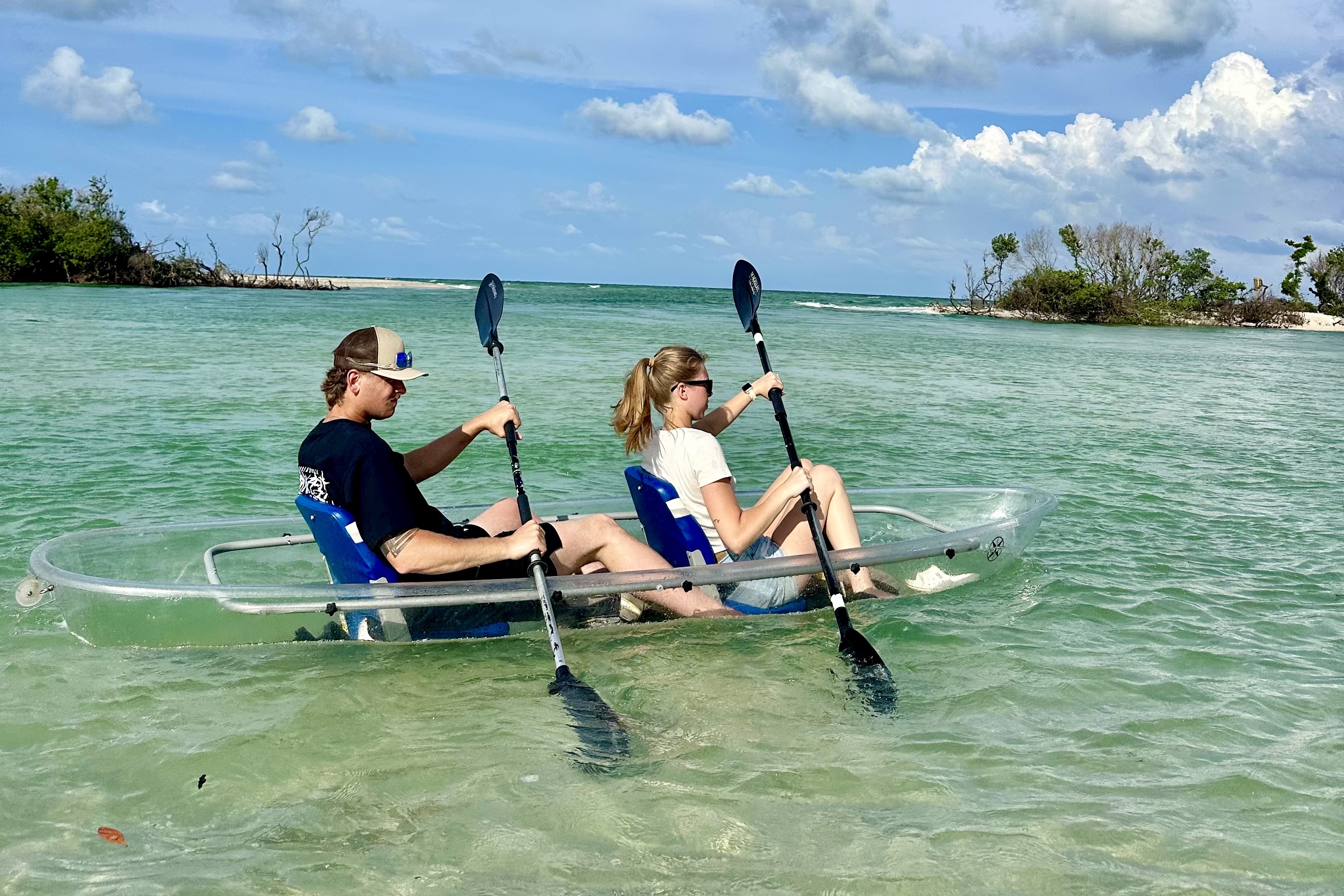 Guests paddling a transparent kayak through shallow Sarasota-area coastal water.