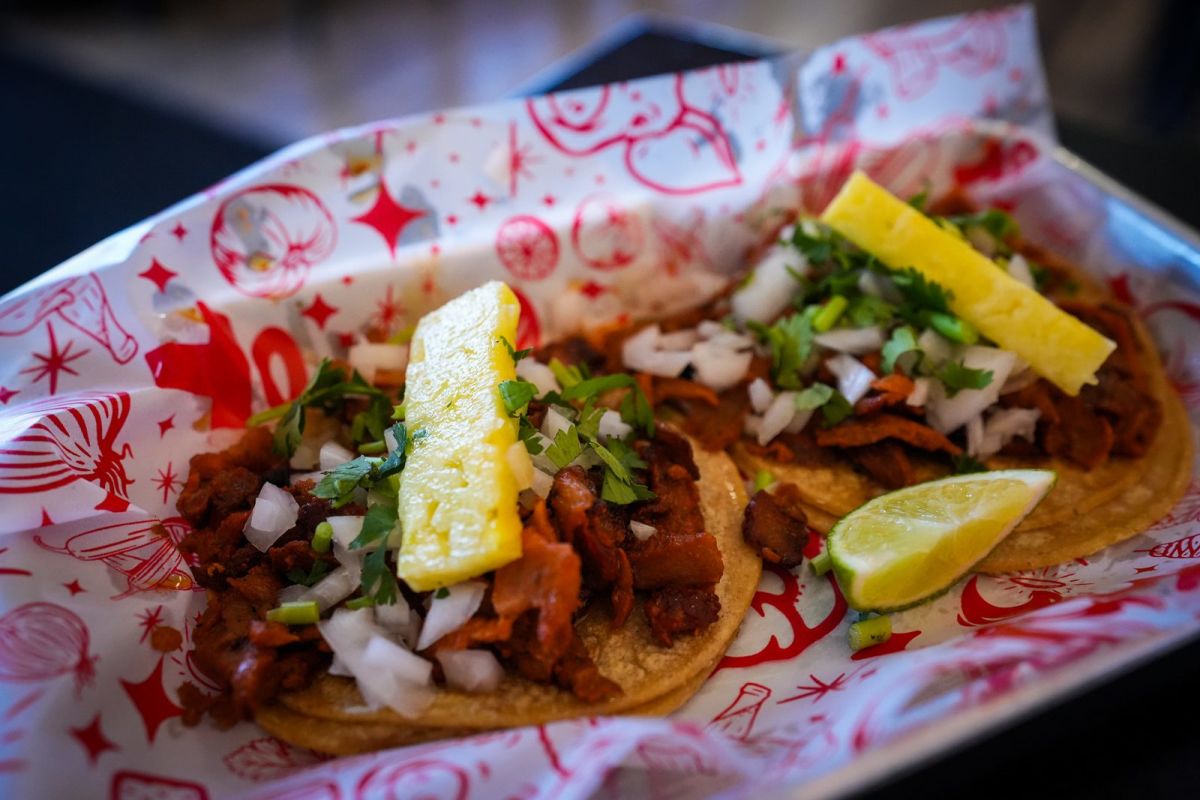 Al pastor tacos topped with pineapple, onion and cilantro in a red basket at Holy Taco