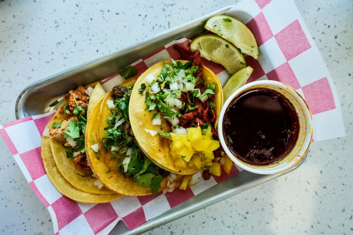 Three street tacos with cilantro and lime beside a cup of consomme on a tray at The Taco Spot in Provo