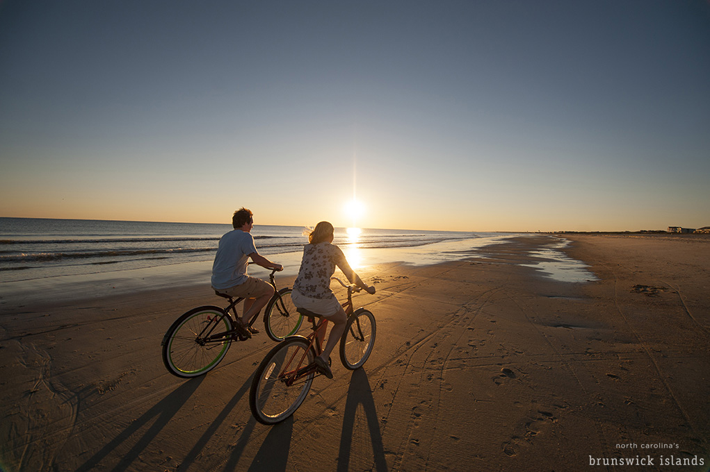 A couple riding bikes on the beach during sunset in the Brunswick Islands