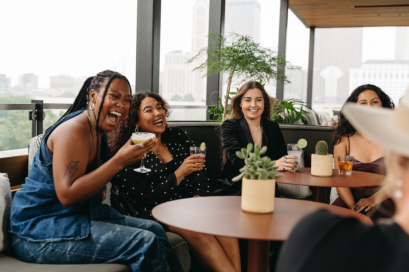 Women sit around table while holding cocktails and laughing at Brass Eye rooftop bar